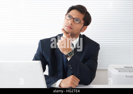 Giovani professionisti uomo ha perso in pensieri con le dita sul mento e guardando verso l'alto nella cabina di office Foto Stock