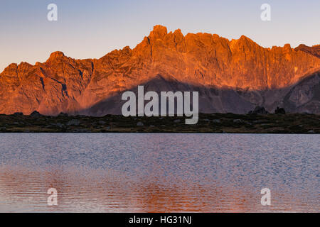 Vista dal lago Laramon. Colore rossastro all'alba sulle vette della Vallée de la Clarée. Crête du Queyrellin picco. Névache. Hautes Alpes. Francia. Foto Stock