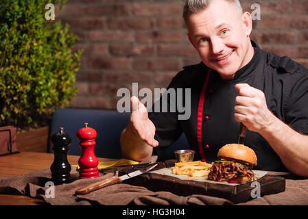 Felice l'uomo mangiare hamburger in ristorante Foto Stock