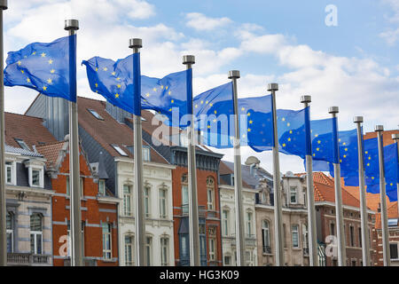 Una linea di Unione europea bandiere su pali di metallo nella parte anteriore dell'edificio Berlaymont a Bruxelles con case tradizionali in background. Foto Stock