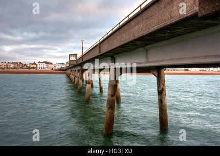 Trattare Pier, in Kent England. Molo di cemento costruire negli anni cinquanta. Vista dalla fine del molo guardando indietro alla spiaggia e la città. Alba nuvole scure nel cielo. Mare calmo. Foto Stock