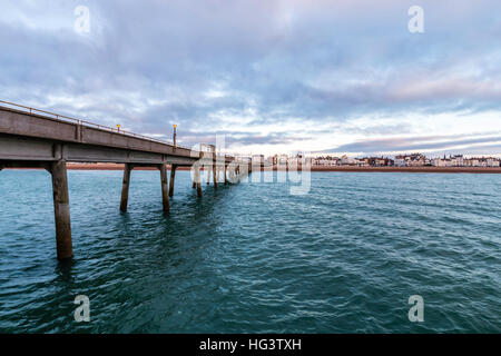 Trattare Pier, in Kent England. Molo di cemento costruire negli anni cinquanta. Vista dalla fine del molo guardando indietro alla spiaggia e la città. Alba nuvole scure nel cielo. Mare calmo. Foto Stock