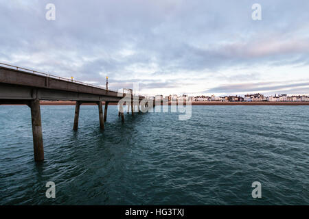 Trattare Pier, in Kent England. Molo di cemento costruire negli anni cinquanta. Vista dalla fine del molo guardando indietro alla spiaggia e la città. Alba nuvole scure nel cielo. Mare calmo. Foto Stock