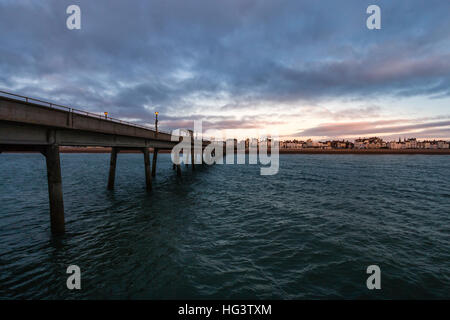 Trattare Pier, in Kent England. Molo di cemento costruire negli anni cinquanta. Vista dalla fine del molo guardando indietro alla spiaggia e la città. Alba nuvole scure nel cielo. Mare calmo. Foto Stock