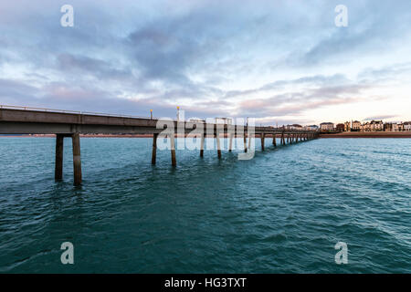 Trattare Pier, in Kent England. Molo di cemento costruire negli anni cinquanta. Vista dalla fine del molo guardando indietro alla spiaggia e la città. Alba nuvole scure nel cielo. Mare calmo. Foto Stock