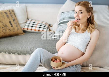 Incinta donna allegra mangiare amaretti Foto Stock