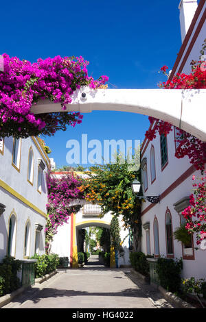 Una tipica strada in Puerto de Mogan con fiori di parete che include purple Bougainvillea intorno gli archi. Foto Stock