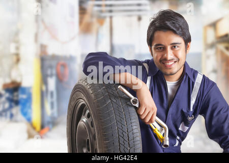 Ritratto di auto meccanico con un pneumatico di ricambio e utensili a mano in garage Foto Stock
