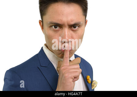 Volto umano espressione. Giovane uomo asiatico in tuta blu mette il dito indice sulle sue labbra esprimendo shh, tranquilla, non fare rumore. Close up ritratto lan del corpo Foto Stock