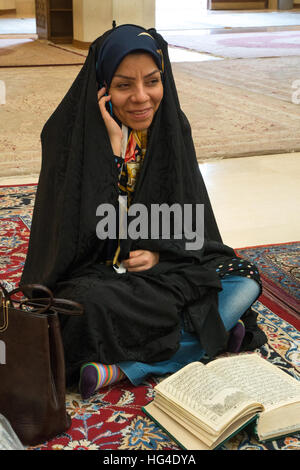 Giovane donna in bilico tra il suo cellulare e la sua lettura religiosa, mausoleo del re di luce, Shiraz, Iran Foto Stock