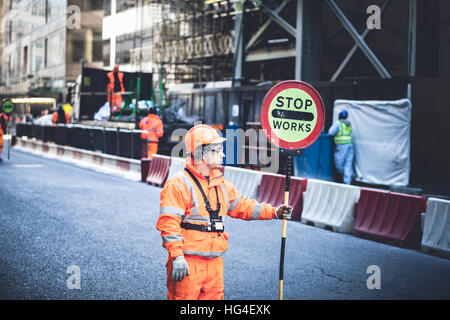 Londra REGNO UNITO, lavoratori bloccando il traffico su strada per le opere con un arresto cartello stradale Foto Stock