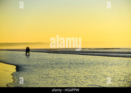 Una giovane coppia in amore tenendo le mani su una spiaggia al tramonto. Foto Stock