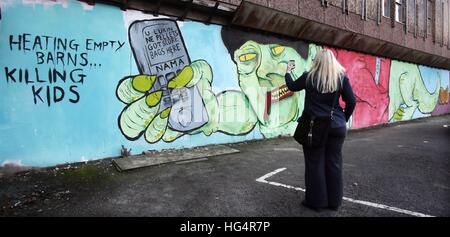 Un membro del pubblico guarda un murale che fa riferimento al calore rinnovabili incentivo (RHI) Crisi e Irlanda del Nord Primo Ministro Arlene Foster in Belfast City Centre parcheggio auto. Foto Stock