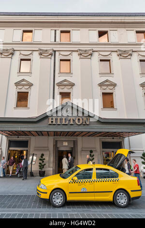 La gente non riconosciuto a piedi nella parte anteriore del parcheggio auto taxi Vicino Hilton Hotel facciata nel quartiere del castello di Buda. Foto Stock