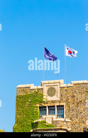 Yonsei University bandiera viola e Taegukgi coreano bandiera nazionale di volare al di sopra una coperta di edera torre di mattoni su un cielo azzurro giorno Foto Stock