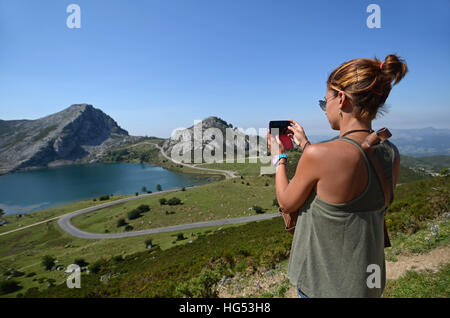 Giovane donna prende una foto dei laghi di Covadonga (Lagos de Covadonga) con il suo telefono cellulare Foto Stock