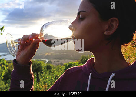 Giovane donna beve vino al tramonto in valle Foto Stock