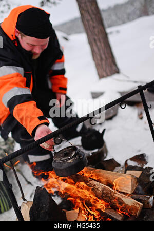 Antti, giovane guida da VisitInari, preparare tè e caffè su un incendio nel deserto del lago Inari, Lapponia, Finlandia Foto Stock