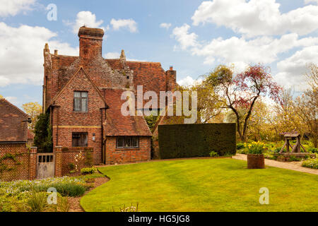 Vecchio rosso mattone cottage inglese nella parte anteriore del prato verde con giardino primaverile, acqua ben Foto Stock