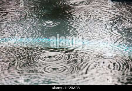 Gocce di pioggia caduta in un corpo di acqua la creazione di schizzi e anelli Foto Stock