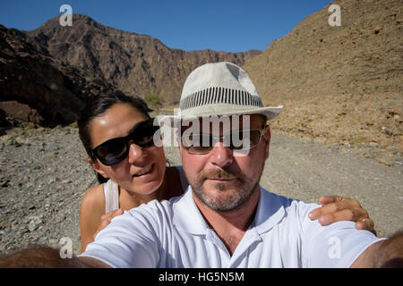 Coppia felice di 40 anni che scatta un selfie grandangolare in un wadi, catturando la loro avventura, la loro esperienza di viaggio e l'emozione in Medio Oriente Foto Stock
