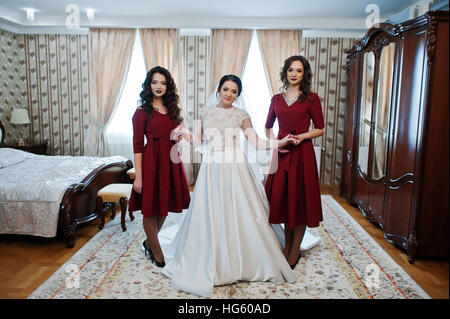 Sposa con due fantastici bridesmaids sul vestito rosso posto sulla camera al giorno di nozze. Foto Stock