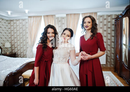 Sposa con due fantastici bridesmaids sul vestito rosso posto sulla camera al giorno di nozze. Foto Stock