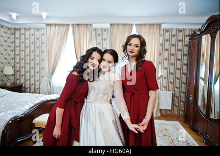 Sposa con due fantastici bridesmaids sul vestito rosso posto sulla camera al giorno di nozze. Foto Stock