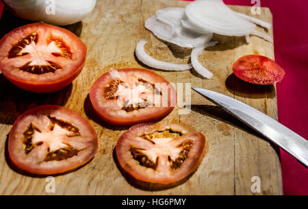 Fotografia di un coltello, le fette di pomodoro e cipolla in un legno tagliere Foto Stock