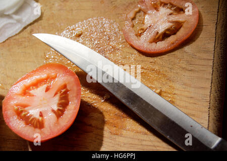 Fotografia di un coltello, le fette di pomodoro e cipolla in un legno tagliere Foto Stock