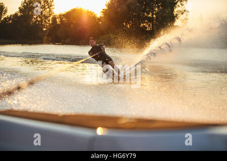 L'uomo Wakeboard sul lago dietro la barca. Sci d'acqua sul lago al tramonto. Foto Stock