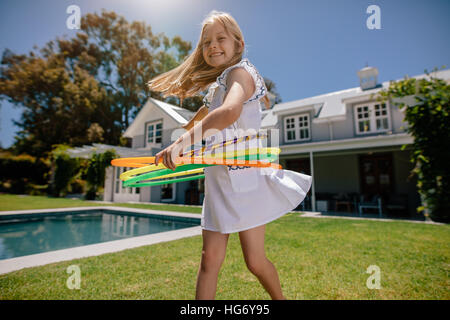 Felice bambina gioca con hula hoop nel cortile. Sorridente ragazza che gioca all'aperto su un giorno d'estate. Foto Stock