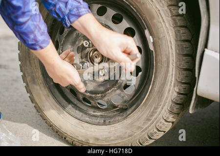 L'uomo la sostituzione di una ruota sulla strada. sul modo in cui vi è stata la rottura della ruota, forare necessarie per sollevare la vettura martinetto e togliere la ruota svitando le n Foto Stock