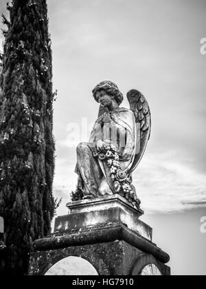 Un angelo inginocchiato statua in pietra a spiovente continua a vegliare su di un grave al di sotto. Foto Stock