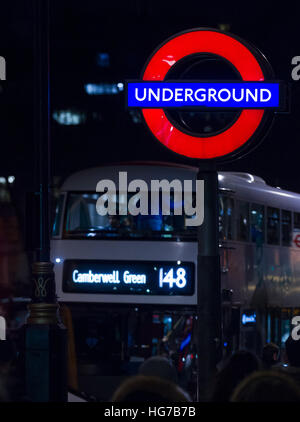 Illuminata London Underground roundel segno del tubo durante la notte con una Londra boris autobus in Piazza del Parlamento, Stazione di Westminster Foto Stock