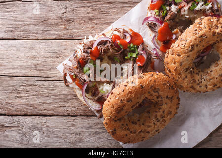 Bagel con tirato il maiale, le cipolle cavolo e salsa sul tavolo. vista orizzontale dal di sopra Foto Stock