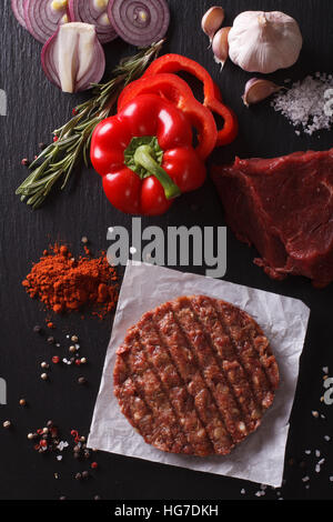 Materie di macinato di manzo hamburger di carne costolette di manzo con ingredienti sulla scheda closeup. vista verticale da sopra Foto Stock