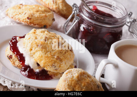 Pasticceria inglese: scones con marmellata e tè con latte vicino sul tavolo. Posizione orizzontale Foto Stock