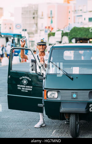Un uomo anziano che indossa un marinaio uniformi della prossima ad una a tre ruote "Ape" veicolo sull'isola di Ponza, Italia Foto Stock