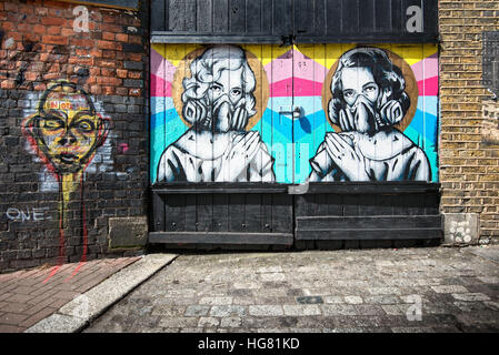 Arte di strada di due donne con le bombolette spray e le maschere su una porta di garage a Londra Foto Stock