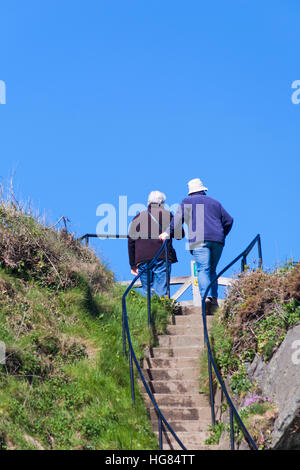 La coppia matura raggiunge la cima dei gradini dall'ufficio del Master dell'Harbour al porto di Porthgain Pembrokeshire Coast National Park, Galles, Regno Unito a maggio Foto Stock