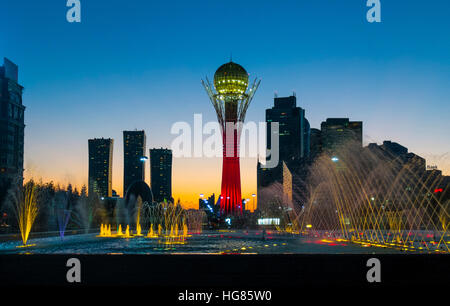 Illuminato Torre di Bayterek e fontana in città contro il cielo blu chiaro Foto Stock