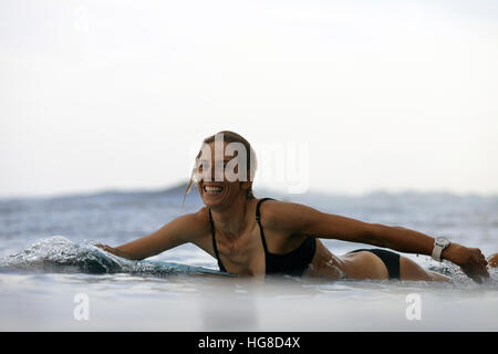 Ritratto di donna felice giacente sulla tavola da surf in spiaggia contro sky Foto Stock