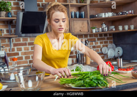 Attraente giovane donna tenendo le cipolle verdi in cucina Foto Stock