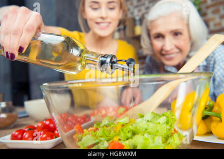 La nipote e nonna cucinare insieme e versando olio in insalata di verdure Foto Stock