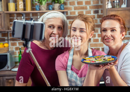 Famiglia di tre generazioni rendendo selfie tenendo la piastra con biscotti di Natale Foto Stock