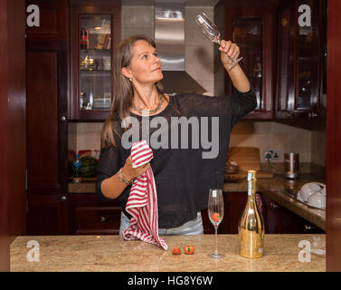 Donna di mezza età pulizia bicchieri da champagne con un rosso asciugamano da cucina. Foto Stock