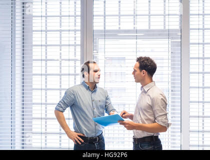 Due colleghi parlare insieme sui documenti di progetto in piedi nel moderno e luminoso interno di office Foto Stock