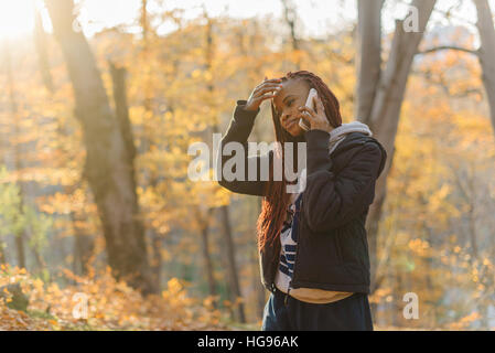 Carino ragazza africana in piedi nel parco autamn e parla al telefono. Donna ha un resto su aria fresca. Ella mise la sua mano sulla testa Foto Stock