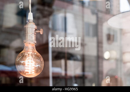 Decorativo Edison vecchio stile lampadina luce contro sfocata scena urbana sfondo riflettente Foto Stock